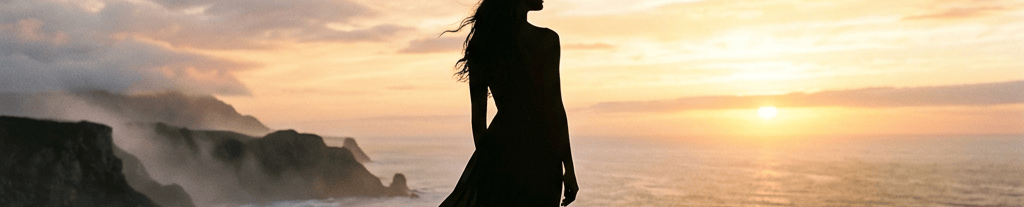 Silhouette of a woman in a flowing dress overlooking the sunset ocean